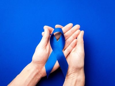 Blue prostate ribbon. Awareness prostate cancer of men health in November. Blue ribbon in hands isolated on deep blue background. November and International Mens Day