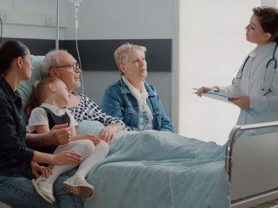 Medic explaining diagnosis to old patient and family in visit, sitting in hospital ward bed. Senior man talking to general practitioner about treatment and medicine, having people visiting.
