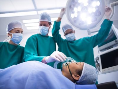 Surgeons adjusting oxygen mask on patient mouth in operation theater of hospital